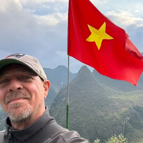 Chad wearing a cap in front of mountains and a Vietnamese flag