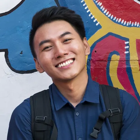 Khoai Lang Thang smiling in front of a colorful wall