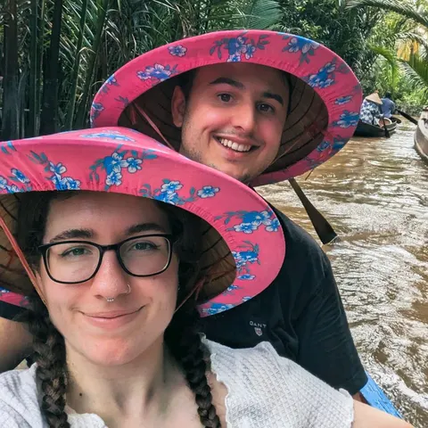 Liam and Sarah wearing colorful hats on a boat in Vietnam